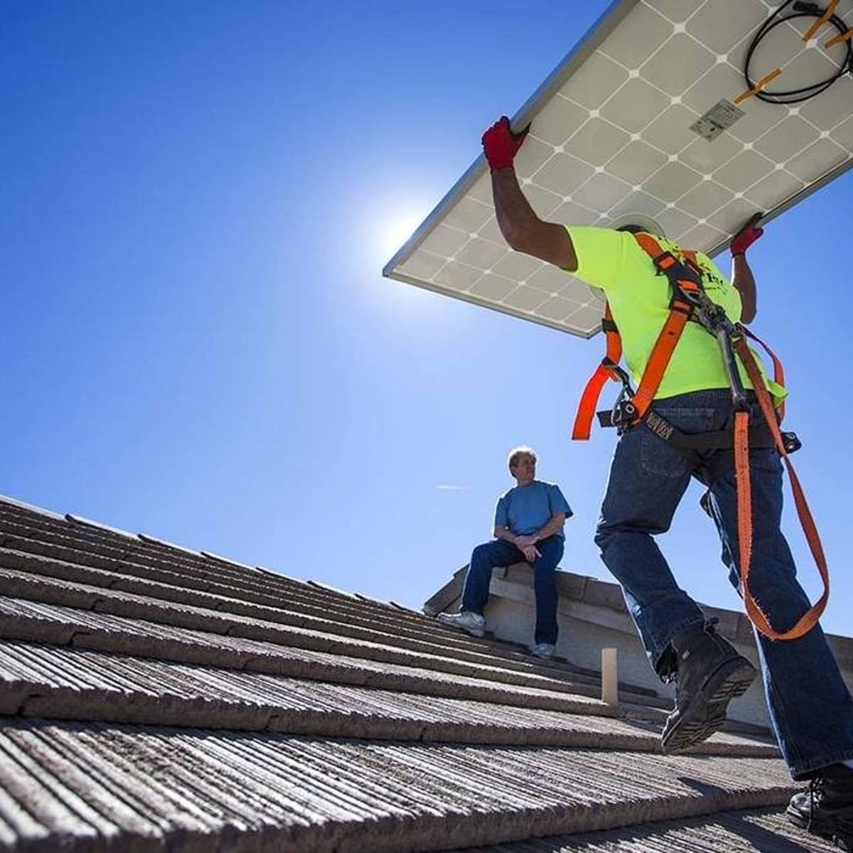 Installer carrying a solar panel up a residential tile roof