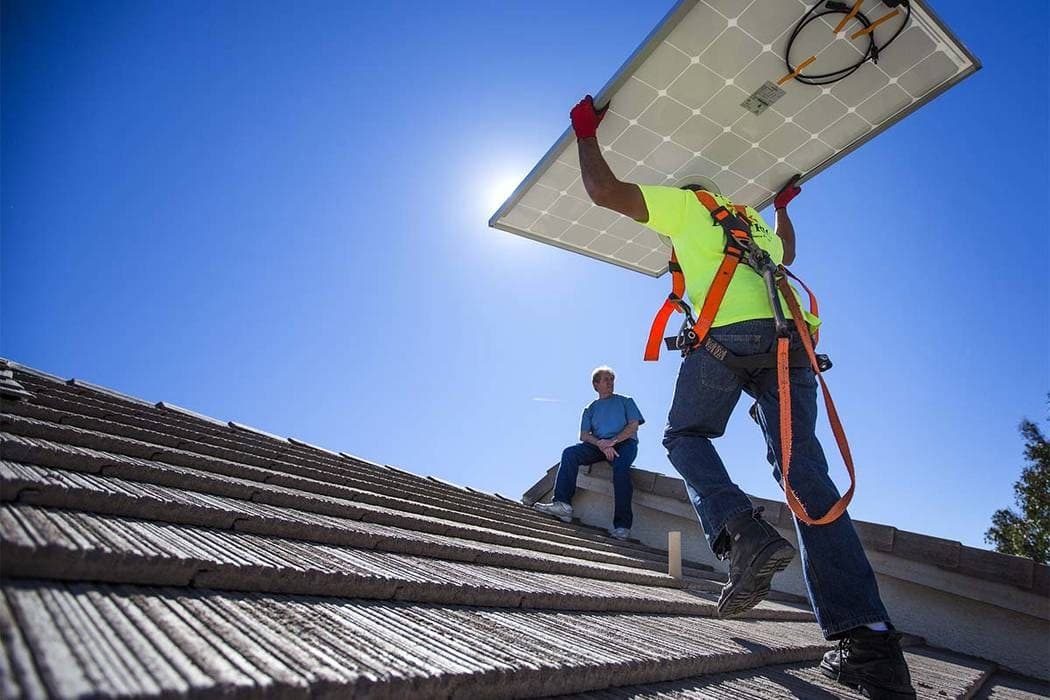 Installer carrying a solar panel up a residential tile roof